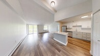 Located at 1 Kimball Ct in Woburn, MA, this three-bedroom, two-bathroom residence offers a thoughtfully designed single-floor layout that balances comfort and modern style. The open-concept living and dining area immediately impresses with soaring vaulted ceilings and wide-plank hardwood flooring, creating a bright and airy atmosphere. Large sliding glass doors lead to a balcony, inviting generous natural light and lush tree-lined views into the space. The kitchen is well-appointed with white shaker cabinetry, light quartz countertops, a central island, and a full suite of stainless steel appliances including a refrigerator, dishwasher, and range. The three bedrooms are carpeted for comfort, each featuring windows that frame verdant outdoor views, with the spacious primary bedroom offering a particularly comfortable retreat. The two bathrooms are finished with clean, modern details — one featuring elegant marble-style tile surrounding a soaking tub with brushed gold fixtures, the other offering a bright vanity and tile flooring. A connecting hallway ties the layout together efficiently. Throughout the home, baseboard heating and individual climate units ensure year-round comfort, while the overall neutral palette provides a versatile, move-in-ready canvas.