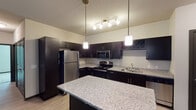 Located in Wyoming, Michigan, this single-floor unit offers a thoughtfully designed layout with contemporary finishes throughout. The kitchen is a standout feature, showcasing rich dark cabinetry, light granite countertops, a full suite of stainless steel appliances including a refrigerator, electric range, microwave, and dishwasher, as well as a double stainless sink and a distinctive diamond-pattern wine rack. Pendant and track lighting illuminate the space, and a central island provides additional counter space and storage. The open-concept living area flows seamlessly from the kitchen, featuring light-toned luxury vinyl plank flooring and a ceiling fan, creating a bright and airy atmosphere. The bedrooms are carpeted for comfort, each equipped with ceiling fans, and at least one benefits from a pair of windows that invite natural light and outdoor views. The bathrooms are finished with granite-topped dark vanities, light vinyl plank flooring, and full tub-shower combinations with curved chrome curtain rods. Neutral wall tones and dark accent doors and trim carry a cohesive modern aesthetic throughout the entire space.