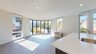 Located at 1725 SW Salmon St in Portland's vibrant West End neighborhood, this contemporary single-floor residence showcases thoughtful modern design throughout. The open living area is defined by a striking curved wall of floor-to-ceiling windows that flood the space with natural light and offer expansive views of the surrounding cityscape and tree-lined streets. Wood-look flooring flows seamlessly throughout, complementing the clean white walls and recessed lighting.

The chef's kitchen is a standout feature, appointed with dark flat-front cabinetry, quartz countertops, a large center island with an integrated sink, stainless steel appliances including a gas range and French door refrigerator, and a geometric hexagonal tile backsplash. Large windows within the kitchen continue the theme of abundant natural light.

The bedroom is generously proportioned with its own window providing views and natural light, along with a wall-mounted HVAC unit for individualized climate control. Two bathrooms mirror the home's modern aesthetic, each featuring dark wood vanities, white quartz countertops, and wood-look tile flooring. A dedicated laundry closet with stacked washer and dryer adds everyday convenience to this well-appointed urban residence.