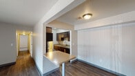 Located at 3800 Pine Terrace Blvd in Kalamazoo, Michigan, this single-floor unit offers a practical and functional layout designed for comfortable everyday living. The living area is bright and open, featuring dark hardwood-style flooring, a wall-mounted air conditioning unit, and a large sliding glass door fitted with vertical blinds that allow natural light to fill the space. Adjacent to the living area, a compact dining space includes a peninsula-style countertop that connects seamlessly to the kitchen. The galley kitchen is well-appointed with rich dark wood cabinetry, light stone-finish countertops, stainless steel appliances including a refrigerator, electric range, and built-in microwave, as well as a double stainless steel sink and additional storage throughout. The carpeted bedroom offers a quiet retreat with neutral wall tones and a window with blinds that provides natural light. The full bathroom features a single-sink vanity with a dark wood cabinet base, a large mirror, and a tub-shower combination with clean white surrounds. A hallway connects the main living spaces, and the overall interior maintains a cohesive, neutral color palette with textured ceilings throughout, creating a clean and move-in-ready environment.