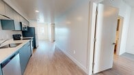 This well-appointed 2-bedroom, 2-bathroom single-floor unit offers a clean, modern aesthetic throughout. Light wood-tone flooring runs continuously across the space, complementing the crisp white walls and creating a bright, cohesive atmosphere.

The open-concept kitchen and living area forms the heart of the unit. The kitchen features sleek blue-grey cabinetry on a single galley-style wall, white countertops, and a full suite of stainless steel appliances including a refrigerator, range, microwave, and dishwasher. Recessed lighting illuminates the kitchen, which flows seamlessly into the living area. The living room benefits from a ceiling fan, a sliding glass door that opens to a private balcony, and an additional window that draws in abundant natural light and outdoor views.

A hallway connects the living area to the two bedrooms and bathrooms. The primary bedroom is a well-proportioned room with direct access to a closet. The second bedroom features a large window that fills the room with natural light. Both bathrooms are finished with clean white walk-in showers with chrome fixtures. A dedicated hallway closet provides additional storage. The overall design is contemporary and functional, with a neutral palette that offers a versatile canvas throughout.