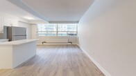This thoughtfully designed 1-bedroom, 1-bathroom unit offers a clean, modern aesthetic across a single floor, with light hardwood flooring and a neutral color palette unifying every room. The open living area is a standout feature, anchored by a wide bank of windows that floods the space with natural light and provides views of the surrounding neighborhood. A panel radiator runs beneath the windows, ensuring year-round comfort, while a textured ceiling adds subtle architectural character.

The kitchen is efficiently laid out with crisp white shaker-style cabinetry, white quartz countertops, a classic subway tile backsplash, and a full suite of stainless steel appliances including a dishwasher, electric range, and over-the-range microwave — ideal for everyday cooking and entertaining.

The spacious primary bedroom accommodates a large furniture arrangement with ease and includes a built-in sliding-door closet for ample storage. A window draws in natural light, while the same warm hardwood flooring continues seamlessly from the rest of the unit.

The bathroom features a full soaking tub and shower combination framed by white subway tile, complemented by a clean white vanity. A dedicated in-unit laundry area with a stacked Bosch washer and dryer adds everyday convenience. A connecting hallway ties all rooms together for a functional and cohesive floor plan.