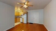 This single-floor unit offers a well-organized layout that maximizes its compact footprint. The open living area is anchored by warm hardwood flooring and a ceiling fan with integrated lighting, creating a comfortable and airy atmosphere. A six-panel entry door provides a clean transition into the space.

The kitchen flows directly from the living area and features honey-toned wood cabinetry with arched detailing, dark granite countertops, a corner sink, a gas range, a full-size refrigerator, and an over-the-range microwave. Light tile flooring distinguishes the kitchen zone from the hardwood in the living area, and a track lighting fixture illuminates the workspace effectively.

The bathroom is finished with neutral floor-to-ceiling tile and includes a pedestal sink, a mirrored medicine cabinet with overhead lighting, a wall-mounted towel ring, and a combined tub and shower with a rainfall-style showerhead — all in a clean, classic arrangement.

The bedroom is bathed in natural light through a pair of windows with outdoor greenery views. Hardwood flooring continues throughout, and a ceiling fan adds comfort. A sliding mirrored closet provides practical storage. The room's soft wall color and bright, open feel make it a relaxing retreat.