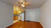 This single-floor unit offers a well-organized layout that maximizes its compact footprint. The open living area is anchored by warm hardwood flooring and a ceiling fan with integrated lighting, creating a comfortable and airy atmosphere. A six-panel entry door provides a clean transition into the space.

The kitchen flows directly from the living area and features honey-toned wood cabinetry with arched detailing, dark granite countertops, a corner sink, a gas range, a full-size refrigerator, and an over-the-range microwave. Light tile flooring distinguishes the kitchen zone from the hardwood in the living area, and a track lighting fixture illuminates the workspace effectively.

The bathroom is finished with neutral floor-to-ceiling tile and includes a pedestal sink, a mirrored medicine cabinet with overhead lighting, a wall-mounted towel ring, and a combined tub and shower with a rainfall-style showerhead — all in a clean, classic arrangement.

The bedroom is bathed in natural light through a pair of windows with outdoor greenery views. Hardwood flooring continues throughout, and a ceiling fan adds comfort. A sliding mirrored closet provides practical storage. The room's soft wall color and bright, open feel make it a relaxing retreat.