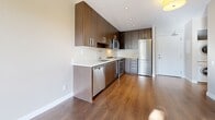 Located at 1515 W 57th Ave in Vancouver, BC, this well-designed one-bedroom, one-bathroom unit offers a thoughtful layout across a single floor. The contemporary kitchen is a standout feature, showcasing rich dark-toned cabinetry that extends to the ceiling for ample storage, white quartz countertops, a clean tile backsplash, and a full suite of stainless steel appliances including a dishwasher, range, over-the-range microwave, and refrigerator. Warm hardwood flooring runs throughout the main living and kitchen areas, adding a sense of cohesion and elegance to the open-concept space. The bedroom is a cozy retreat, finished with plush carpet and featuring a large floor-to-ceiling window that invites abundant natural light and offers pleasant views of surrounding greenery. A mirrored sliding closet adds both functionality and the illusion of additional space. The bathroom is finished with neutral tones, featuring light tile flooring, a dark wood vanity with a white countertop, a modern chrome faucet, and wall-mounted lighting above a large mirror. Clean lines and a neutral palette throughout the unit create a calm, modern ambiance well-suited for comfortable urban living.