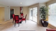 This single-floor residence is thoughtfully designed with a cohesive neutral color palette and consistent finishes throughout. The living room provides a comfortable gathering space with plush carpeting, crown molding, and a textured ceiling, accommodating both a sofa and lounge seating alongside open shelving for display and storage. Large windows allow natural light to filter in, and a wall mirror enhances the sense of space.

The adjacent dining area features sliding glass doors that open directly onto a private balcony, offering outdoor views and additional natural light. The kitchen is galley-style, equipped with granite-look countertops, a double-basin stainless steel sink, dark wood cabinetry, tile flooring, and black appliances including an electric range.

The primary bedroom includes a tray ceiling with a ceiling fan, carpet flooring, and a generously sized window overlooking greenery. A second bedroom is similarly carpeted and bright, with an en-suite bathroom featuring a tub-shower combination and a vanity with dark wood cabinetry. A second full bathroom with a tub-shower and white fixtures serves the remainder of the unit. Throughout the residence, warm beige tones, carpet in living and sleeping areas, and tile in wet areas create a cohesive and functional interior.