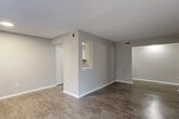 This single-story home is thoughtfully arranged across a generously sized floor plan, accommodating four bedrooms, one full bathroom, a combined kitchen and living area, a hallway, and two closets. The interior features a neutral gray and beige color palette throughout, complemented by wood-look hard flooring in the main living areas and kitchen, and plush carpet in select bedrooms.

The open living room is spacious and well-lit, connecting seamlessly to the kitchen via a pass-through window. The galley-style kitchen is equipped with white cabinetry, light stone-look countertops, a stainless steel sink, and black appliances including a refrigerator, dishwasher, and electric range. A textured ceiling is consistent throughout the home, adding a classic character.

The bedrooms vary in size, with the primary bedroom offering notable space and a sliding glass door that opens to an outdoor view of surrounding greenery, providing a private, nature-facing retreat. Additional bedrooms feature carpeted floors and standard closet access. The shared bathroom includes wood-look flooring and connects conveniently to the hallway. A central hallway links all rooms, ensuring a practical and efficient flow throughout the home.