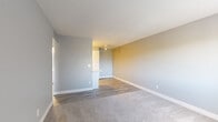 Located at 5555 E 14th St in Tucson, Arizona, this one-bedroom, one-bathroom unit offers a practical and comfortable single-floor layout. The living room features a combination of plush carpeting and wood-look vinyl flooring, neutral gray and beige wall tones, and a ceiling fan overhead. A built-in counter or pass-through area connects to the adjacent space, adding a functional architectural detail. Natural light filters in through windows dressed with vertical blinds, lending a bright and airy feel throughout. The bedroom is a well-proportioned, carpeted retreat with soft gray walls, a window that brings in natural light, and overhead ventilation via ceiling vents. It opens through a hallway to a dedicated closet with built-in shelving, offering organized storage. The full bathroom is clean and efficient, featuring wood-look tile flooring, a white vanity with a single-basin sink, a tub and shower combo with a standard curtain rod, and a wall mirror. White baseboards throughout the unit provide a crisp, consistent finish. The hallway connects all rooms in a straightforward layout, making the space easy to navigate. Overall, the unit presents a tidy, neutral aesthetic well-suited for practical everyday living in the heart of Tucson.