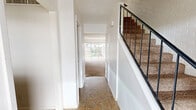 This two-story home offers a practical and well-organized layout spread across two floors. The main level features an entry hallway with tile flooring that leads into the primary living areas. The living room is a generously sized space with plush carpeting, a ceiling fan, and large sliding glass doors that open to an outdoor patio and fenced backyard, allowing ample natural light and outdoor views. Adjacent to the living room, the kitchen is equipped with rich wood cabinetry, a white subway tile backsplash, a built-in oven, dishwasher, and a window that brings in natural light. The main floor also includes a closet with built-in shelving and washer/dryer hookups, adding practical utility. A carpeted staircase with a black metal railing leads to the upper level, where both bedrooms are located. The spacious primary bedroom features carpet flooring, a wide window with outdoor views, and a wall-mounted light fixture. The second bedroom is equally comfortable, with soft carpet and a window overlooking the exterior. A full bathroom and hallway complete the upper floor. Throughout the home, white walls, textured ceilings, and neutral tones create a clean, understated aesthetic.