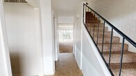 This two-story home offers a practical and well-organized layout spread across two floors. The main level features an entry hallway with tile flooring that leads into the primary living areas. The living room is a generously sized space with plush carpeting, a ceiling fan, and large sliding glass doors that open to an outdoor patio and fenced backyard, allowing ample natural light and outdoor views. Adjacent to the living room, the kitchen is equipped with rich wood cabinetry, a white subway tile backsplash, a built-in oven, dishwasher, and a window that brings in natural light. The main floor also includes a closet with built-in shelving and washer/dryer hookups, adding practical utility. A carpeted staircase with a black metal railing leads to the upper level, where both bedrooms are located. The spacious primary bedroom features carpet flooring, a wide window with outdoor views, and a wall-mounted light fixture. The second bedroom is equally comfortable, with soft carpet and a window overlooking the exterior. A full bathroom and hallway complete the upper floor. Throughout the home, white walls, textured ceilings, and neutral tones create a clean, understated aesthetic.