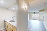 This thoughtfully designed 1-bedroom, 1-bathroom unit offers a functional and comfortable single-floor layout. Light wood-look flooring runs throughout the main living areas, creating a clean, cohesive aesthetic complemented by neutral warm-beige walls and white trim.

The open living room is bright and airy, anchored by a large picture window that frames urban views and fills the space with natural light. A wall sconce adds a decorative accent near the kitchen transition. The living area connects seamlessly to a galley-style kitchen featuring light maple cabinetry, white quartz countertops, a stainless steel sink, and a full suite of stainless steel appliances including a refrigerator, electric range, over-the-range microwave, and dishwasher.

The bedroom is a comfortably sized retreat with its own large window overlooking greenery, hardwood-style flooring, and access to a private balcony through a glass door, allowing for additional natural light and outdoor air.

The bathroom features elegant large-format marble-look tile flooring, a full tub-shower combination, a toilet, and a vanity with ample cabinetry. A hallway connects the main rooms, providing a practical flow throughout the unit. Overall, the space presents a modern, move-in ready environment with clean finishes and thoughtful details throughout.