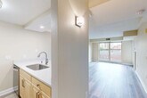 This thoughtfully designed 1-bedroom, 1-bathroom unit offers a functional and comfortable single-floor layout. Light wood-look flooring runs throughout the main living areas, creating a clean, cohesive aesthetic complemented by neutral warm-beige walls and white trim.

The open living room is bright and airy, anchored by a large picture window that frames urban views and fills the space with natural light. A wall sconce adds a decorative accent near the kitchen transition. The living area connects seamlessly to a galley-style kitchen featuring light maple cabinetry, white quartz countertops, a stainless steel sink, and a full suite of stainless steel appliances including a refrigerator, electric range, over-the-range microwave, and dishwasher.

The bedroom is a comfortably sized retreat with its own large window overlooking greenery, hardwood-style flooring, and access to a private balcony through a glass door, allowing for additional natural light and outdoor air.

The bathroom features elegant large-format marble-look tile flooring, a full tub-shower combination, a toilet, and a vanity with ample cabinetry. A hallway connects the main rooms, providing a practical flow throughout the unit. Overall, the space presents a modern, move-in ready environment with clean finishes and thoughtful details throughout.