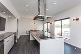 This contemporary single-floor space is thoughtfully designed with a clean, modern aesthetic throughout. The open-concept lounge serves as the centerpiece, featuring a tufted caramel leather sofa, a wall-mounted fireplace, and a flat-screen TV — all set against crisp white walls and durable wood-toned flooring. Large sliding glass doors and floor-to-ceiling windows flood the lounge with natural light while offering direct views of and access to a furnished outdoor terrace, where city skyline views can be enjoyed. Recessed lighting and modern wall sconces complement the airy ambiance.

The dining area is equally refined, anchored by a solid walnut-toned table surrounded by cognac leather chairs. A striking multi-globe brass chandelier adds a contemporary design accent, and a sliding glass door connects the space to the outdoor terrace with a gas grill. The kitchen is outfitted with stainless steel appliances, an island with a cooktop and overhead range hood, gray quartz countertops, white cabinetry, and a wall-mounted TV — making it as functional as it is stylish. Together, these spaces create a versatile, well-appointed environment ideal for gathering, dining, and entertaining.