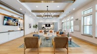 This single-floor community space showcases a refined modern farmhouse design that seamlessly blends comfort and style. The main lounge area commands attention with its soaring ceilings adorned with exposed wood beams, a shiplap ceiling detail, and a striking wrought-iron candle-style chandelier that serves as a central focal point. Light hardwood flooring runs throughout, unifying the open layout with warmth and continuity.

The generous seating area features an eclectic mix of upholstered armchairs, a tufted leather sofa, and round ottomans arranged around a stone-top coffee table atop a layered area rug. A built-in media wall with white cabinetry, a whitewashed brick surround, and wood shelving provides an entertainment focal point for the lounge.

A dedicated coffee bar area is outfitted with light gray cabinetry, granite countertops, a matte black faucet, and a geometric-patterned tile backsplash, offering a welcoming refreshment station. A compact private meeting room features a whitewashed exposed brick accent wall, industrial-style wall sconce lighting, and a round table with wood chairs — ideal for small gatherings or focused work sessions.

Banks of large multi-pane windows line the perimeter walls, flooding the entire space with abundant natural light and offering views of lush surrounding greenery, enhancing the bright and inviting atmosphere throughout.