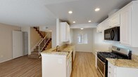 This two-story residence is thoughtfully designed across two levels, offering a functional layout with updated finishes throughout. The main level centers around an open-concept kitchen and living area. The kitchen is well-appointed with white shaker-style cabinetry, granite countertops, a stainless steel gas range, built-in microwave, and a peninsula with a sink that overlooks the adjacent spaces. Light wood-style flooring flows throughout the main level, complementing the neutral wall tones and recessed lighting overhead.

The living area is generously sized and filled with natural light from a sliding glass door that opens to an outdoor area with views of surrounding greenery. A ceiling fan adds comfort to the space. A staircase with white balusters connects the main level to the upper floor.

Upstairs, the bedrooms feature plush carpeting, vertical-blind windows that bring in natural light, and mirrored closet doors. The bathrooms on both levels are finished with granite-topped white vanities, large mirrors, and combination tub-shower setups. Textured ceilings are consistent throughout the home, adding a classic residential character to every room.