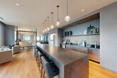 Located in the heart of Midtown Atlanta, this generously scaled single-floor amenity space offers a sophisticated blend of social and private environments. Warm hardwood flooring — including striking herringbone-patterned sections — flows throughout, unifying the varied zones with a sense of cohesion and elegance.

The entertainment area anchors the space with a full-size billiards table beneath globe pendant lights, set against bold teal accent walls and flanked by a two-sided fireplace that opens to a stylishly furnished lounge. A dedicated wet bar and kitchen area features a dramatic stone-topped island with bar seating, dark wood cabinetry, a textured tile backsplash, and a row of globe pendants descending from the ceiling.

The dining room offers floor-to-ceiling windows with panoramic views of the Atlanta skyline, a wood-paneled ceiling, and a mix of lounge and café-style seating. Glass-partitioned private rooms provide quieter settings for focused work or intimate gatherings, with views to the exterior. A built-in wine storage wall and workstation nook add functional elegance. The hallway connects zones seamlessly, while curated artwork and lush greenery enhance the upscale, welcoming ambiance throughout.