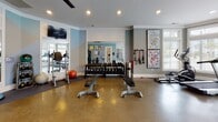 Located at 2451 Margarita Dr in Myrtle Beach, SC, this single-story fitness center is thoughtfully designed to support a comprehensive workout experience. The space is divided into distinct functional zones, each catering to different aspects of exercise. A standout feature is the bay window area, where a sweeping arrangement of floor-to-ceiling windows floods the cardio zone with natural light and offers views of an outdoor pool, creating an inviting atmosphere for treadmill and elliptical workouts. A modern ceiling fan overhead aids in ventilation and comfort.

The strength training area is well-appointed with a full dumbbell rack, adjustable weight benches, resistance bands, a cable machine, and additional resistance equipment. Large wall-mounted mirrors expand the visual depth of the space and allow users to monitor their form during workouts. The polished concrete floors are durable and easy to maintain throughout both zones.

Soft blue accent walls contrast with crisp white trim and recessed lighting, lending the space a clean, contemporary aesthetic. Decorative artwork adds a touch of personality, while a wall-mounted television provides entertainment. A hand sanitizer station and towel station further enhance the functionality of this well-maintained fitness facility.