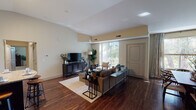 This well-appointed two-bedroom, two-bathroom residence spans a generous single floor, thoughtfully designed to maximize both comfort and functionality. Rich, dark hardwood flooring flows throughout the main living areas, complemented by vaulted ceilings that lend an open, airy feel to the space.

The living room is a bright, welcoming retreat anchored by floor-to-ceiling sliding glass doors that flood the room with natural light and provide direct access to a private balcony overlooking lush greenery. The adjacent dining area features vaulted ceilings and a large window framed by elegant draping, creating an intimate yet luminous setting for meals.

The kitchen is well-equipped with dark espresso cabinetry, granite countertops, stainless steel appliances, and a curved breakfast bar ideal for casual dining. Track lighting overhead enhances both style and practicality.

The bedrooms offer a calm, neutral palette with plush carpeting. One bedroom features high clerestory windows and a sliding-door closet with built-in shelving, providing ample storage. The bathrooms mirror the kitchen's refined aesthetic with granite vanity tops, dark wood cabinetry, and framed mirrors. This residence combines modern finishes with a warm, cohesive design throughout.