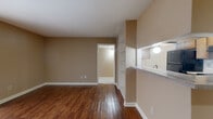 Located at Windchase Apartments in Houston, TX, this one-bedroom, one-bathroom apartment offers a practical and comfortable single-floor layout. Rich hardwood-style flooring flows throughout the main living areas, adding warmth and cohesion to the space. The open-concept living room is bright and inviting, featuring neutral beige walls, built-in shelving for display or storage, and a sliding glass door that leads to a private patio with an outdoor view. A pass-through counter connects the living area to the kitchen, which is equipped with wood-tone cabinetry, speckled countertops, a black refrigerator, dishwasher, and range. A bifold pantry door adds additional storage convenience. The bedroom is carpeted for comfort, bathed in natural light through a window with blinds, and features direct access to a spacious walk-in closet outfitted with multi-level hanging rods and shelving. The bathroom includes a tiled shower-tub combo with chrome fixtures, a wood-vanity with granite-style countertop, and hardwood-style flooring. A hallway connects all rooms efficiently, completing this well-organized and functional floor plan ideal for everyday living.