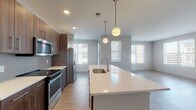 Located at 12 W Gay St in the heart of Columbus, Ohio, this single-floor residence offers a thoughtfully designed open-concept layout with contemporary finishes throughout. The kitchen serves as a focal point of the living space, showcasing rich dark wood cabinetry, white quartz countertops, a subway tile backsplash, and a full suite of stainless steel appliances including a range, microwave, and refrigerator. A large center island with an undermount sink and stylish globe pendant lighting above creates an ideal space for both meal preparation and casual dining. The kitchen flows seamlessly into the spacious living and dining area, which features light wood-look flooring and multiple windows fitted with blinds that invite natural light throughout. The bedrooms are carpeted for comfort and include windows that offer views of the surrounding Columbus streetscape. The bathrooms are finished with the same dark wood vanity cabinetry, white quartz countertops, and wood-look tile flooring. One bathroom features a tub-shower combination with clean white tile surround, while another includes direct access to a walk-in closet. Recessed lighting and neutral tones across all rooms create a clean, cohesive, and modern aesthetic throughout the entire residence.