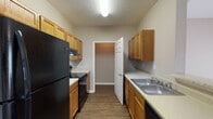 This single-floor unit in Pearl, Mississippi, offers a functional and well-organized layout designed to maximize comfort and usability. The open-concept living area features neutral-toned carpet, a ceiling fan with light fixture, and a seamless connection to the kitchen via a half-wall breakfast bar, creating an inviting shared space suited for everyday living.

The galley-style kitchen is efficiently arranged with warm oak cabinetry lining both walls, providing ample upper and lower storage. Black appliances, including a refrigerator, range, and dishwasher, complement the light countertops, while wood-look flooring adds durability underfoot. A door at the end of the kitchen leads to additional storage space.

The primary bedroom is generously sized with carpeted flooring, a ceiling fan, and French doors that invite natural light and outdoor access. It connects to a private en-suite bathroom featuring a vanity with wood cabinetry, a large mirror, and a full soaking tub. An adjacent walk-in closet with wire shelving provides organized storage.

The second bedroom is carpeted and well-lit by a window with blinds, along with a ceiling fan overhead. The second full bathroom mirrors the quality of the primary bath. Throughout the unit, wood-look flooring anchors the main areas, while warm neutral tones create a cohesive and welcoming ambiance.