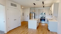 This single-floor unit at 2215 Hickory St in St. Louis, MO offers a clean, contemporary design with an open-concept layout that seamlessly connects the kitchen and living area. The kitchen is a standout feature, outfitted with white shaker-style cabinetry extending to the ceiling for generous storage, a crisp white quartz countertop island, and a full suite of stainless steel appliances including a refrigerator, range, built-in microwave, and dishwasher. A textured tile backsplash adds subtle visual interest, while a cluster of globe pendant lights suspended from a black track rail above the island provides focused, stylish illumination. Track lighting continues throughout the space, complementing recessed ceiling lights.

Light-toned hardwood flooring flows through the kitchen and living areas, creating a warm, cohesive feel. The living area is bright and open, receiving natural light through a set of windows fitted with roller shades. The bedroom features plush carpet and an open closet with built-in shelving for organization. The bathroom maintains the unit's clean aesthetic with white cabinetry, a single vanity, and a tub-shower combination. Overall, the space presents a modern, well-appointed interior suited for comfortable urban living.