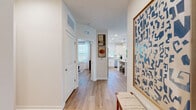 This thoughtfully designed 2-bedroom, 2-bathroom residence offers a cohesive, single-floor layout that maximizes both functionality and comfort. Light wood flooring flows seamlessly throughout, unifying the open-concept living spaces with a warm, contemporary aesthetic.

The kitchen is a standout feature, outfitted with crisp white shaker cabinetry, quartz countertops, a subway tile backsplash, stainless steel appliances, and a central island with bar seating. Pendant lighting and a large window fill the space with natural light, making it as inviting as it is practical.

The open living room is anchored by a bank of oversized windows dressed with sheer white curtains and wood blinds, flooding the room with daylight and creating an airy, comfortable atmosphere. A ceiling fan adds to the functionality of this well-lit gathering space.

The primary bedroom offers a quiet retreat with natural light filtering through large windows, while the second bedroom features a distinctive accent wall in soft blue, ceiling fan, and generous window exposure. Both bedrooms are well-proportioned and relaxing in character.

The bathrooms are finished with white vanity cabinetry, quartz countertops, and wood-look flooring. One bath includes a glass-enclosed walk-in shower with white tile surround and built-in shelving. A hallway with closet storage completes the efficient floor plan.