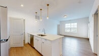 Located at 5155 Raglan St. in Hilliard, Ohio, this well-appointed 2-bedroom, 1-bathroom residence offers a thoughtfully designed single-floor layout with a bright, contemporary aesthetic throughout. The open-concept living and kitchen area serves as the heart of the home, featuring light wood-style flooring, crisp white walls, and a large window that fills the space with natural light. The kitchen is a standout, showcasing a generous white quartz island with an undermount sink, sleek white cabinetry extending to the ceiling, and a full suite of stainless steel appliances including a refrigerator, range, and microwave. Elegant gold pendant lighting adds a modern touch overhead. Both bedrooms are carpeted and well-lit by wide windows with outdoor views, offering a comfortable and quiet retreat. The primary bedroom includes a dedicated closet with built-in shelving for organized storage. The full bathroom is efficiently designed with a double-sink vanity topped in white quartz, a tub-shower combination, and matching wood-style flooring. A dedicated laundry room houses a full-size washer and dryer. A door leading to an exterior balcony area provides convenient outdoor access, completing this functional and stylish residence.