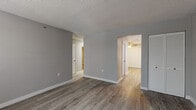 This single-floor residence offers a clean, contemporary aesthetic throughout, unified by grey-toned luxury vinyl plank flooring and neutral grey walls with crisp white trim. The entry area welcomes residents with a bold dark front door and a bright window that allows natural light to fill the space. Textured ceilings are consistent across the unit, adding subtle dimension overhead.

The living area connects openly to the rest of the layout, with a louvered closet providing practical storage. The kitchen is well-equipped with white shaker-style cabinetry, granite-patterned countertops, and a full suite of stainless steel appliances, including an electric range, over-the-range microwave, and dishwasher. Vertical blinds cover a sliding door or window, offering light control.

The bedrooms each feature ceiling fans with integrated lighting, windows with blinds, and louvered closet doors. Two full bathrooms serve the unit, each outfitted with a tub/shower combination, white fixtures, a single-sink vanity with white cabinetry, and coordinating hardware. The overall layout is functional and efficiently organized, with hallways connecting the common areas to the private rooms.