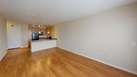 This single-floor residence offers a thoughtfully designed layout that balances functionality and comfort. The open-concept kitchen is a standout feature, equipped with light maple cabinetry, granite-style countertops, and black appliances including a refrigerator, electric range with overhead exhaust, and dishwasher. A peninsula with a double stainless steel sink extends the workspace and serves as a natural divider between the kitchen and the living area. Elegant pendant lighting and track lighting illuminate the kitchen, adding a polished finish. The spacious living area is finished with warm hardwood flooring that flows throughout the common spaces, and large windows with blinds allow natural light to fill the room. A set of French doors provides access to the exterior, enhancing the sense of openness. The bedroom features neutral-toned carpet, a ceiling fan with light fixture, and a window that brings in additional natural light. The bathroom is clean and functional, featuring a framed sliding glass walk-in shower with white tile surround, tile flooring, and brushed nickel grab bars. A dedicated laundry room houses a full-size side-by-side washer and dryer, accompanied by built-in shelving for added storage convenience.