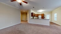 This single-floor residence offers a thoughtfully designed layout that balances comfort and functionality. The open-concept living area is finished with plush wall-to-wall carpeting, crown molding, and a ceiling fan with a light fixture, creating a welcoming and airy atmosphere. The space flows seamlessly into the kitchen, which is visible over a raised breakfast bar counter topped with granite-style countertops. The kitchen is fully equipped with rich cherry wood cabinetry, stainless steel appliances including a range, over-the-range microwave, and refrigerator, all complemented by warm hardwood flooring. A glass-paned door in the kitchen area provides access to the outdoors and allows natural light to fill the space. The bedrooms are generously sized, carpeted, and fitted with ceiling fans, offering a comfortable retreat. One bedroom connects to a spacious walk-in closet outfitted with wire shelving systems on multiple walls for ample storage. The full bathroom features tile flooring, a wood-toned vanity with a broad countertop and mirror, a toilet, and a full tub-shower combination. Crown molding appears consistently throughout, adding a refined architectural detail to every room.
