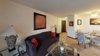 This single-floor residence offers a practical and comfortable layout designed for everyday living. The living room serves as the heart of the space, featuring wall-to-wall carpeting, a sliding glass door that opens to a private balcony with outdoor views of a grassy area, and a wall-mounted air conditioning unit. Natural light fills the room, creating a bright and welcoming atmosphere. The open flow connects the living area to the rest of the unit seamlessly.

The kitchen is efficiently designed with warm oak cabinetry offering generous storage, white countertops, a double-basin stainless steel sink, a dishwasher, and a full-size refrigerator. Tile flooring and overhead lighting make it a clean, functional workspace.

The bedrooms are carpeted and well-proportioned, each featuring vertical blinds over windows that allow for natural light and privacy. One bedroom includes a sliding closet, providing ample storage. The rooms offer a calm, neutral ambiance suited for rest and relaxation.

The bathroom is clean and classic in design, featuring a tiled shower-tub combination, a single vanity with a large mirror, and neutral finishes throughout. A hallway connects the rooms, completing the thoughtful and efficient floor plan of this inviting residence.
