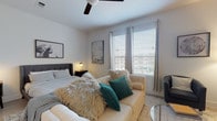 This single-floor, one-bedroom, one-bathroom unit is thoughtfully designed to maximize every square foot of its compact footprint. The open layout seamlessly connects the kitchen, dining, and living areas, creating a cohesive and functional flow throughout the space. Light wood-tone flooring runs throughout, contributing to a clean, contemporary aesthetic.

The galley-style kitchen features rich wood cabinetry, granite-look countertops, a herringbone tile backsplash, and a full suite of stainless steel appliances including a range, microwave, and refrigerator. A narrow bar-height table with stools near the entryway serves as a casual dining area.

The bedroom is generously proportioned for the unit's overall size, accommodating a full sleeping area and a separate seating arrangement. Large windows with blinds and curtain panels allow abundant natural light, while a ceiling fan adds comfort. Warm sconce lighting on either side of the bed enhances the room's cozy ambiance.

The bathroom includes a soaking tub with tiled surround, wood-toned cabinetry with granite countertops, and direct access to a walk-in closet with built-in shelving—providing notable storage capacity for a unit of this scale.