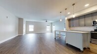 This well-appointed single-floor residence offers a thoughtfully designed open-concept layout that seamlessly connects the kitchen, dining, and living areas. Rich hardwood flooring flows throughout the main living spaces, complemented by neutral gray walls and clean white trim that create a bright, cohesive aesthetic.

The kitchen is a standout feature, showcasing gray shaker-style cabinetry with brushed nickel hardware, white quartz countertops, and a classic subway tile backsplash. A central island provides additional prep and seating space, while pendant lighting above adds warmth and definition. Stainless steel appliances, including a refrigerator, range, microwave, and dishwasher, complete the modern setup.

The expansive living area benefits from multiple windows that invite abundant natural light, and is equipped with a ceiling fan for year-round comfort. The bedrooms are finished with plush carpeting and feature roller shade windows that provide privacy while still allowing light.

The primary bathroom impresses with large-format marble-look tile flooring and a glass-enclosed walk-in shower, exuding a spa-like quality. A secondary bathroom offers a full tub-shower combination with white tile surround and wood-look vinyl flooring. Every detail of this residence reflects a clean, contemporary design sensibility.