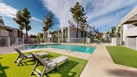 Located at 1750 S Alma School Rd in Mesa, Arizona, this outdoor community space centers around a generously sized swimming pool that serves as the focal point of the property. The pool area is enclosed by a white metal safety fence and features wide concrete pool decking that provides ample space for movement and relaxation. A section of artificial turf adds a vibrant green contrast to the hardscape, and is furnished with lounge chairs and a side table, creating an inviting spot to unwind under the Arizona sun. Outdoor dining seating with a table and umbrella is also available within the fenced area, offering a shaded option for residents. Mature trees — including tall pines and palms — rise above the surrounding buildings, providing natural shade and greenery that softens the desert environment. The surrounding multi-story residential buildings feature a contemporary Southwestern architectural style, with stucco exteriors in muted earth tones accented by green trim and geometric massing. The open layout of the pool courtyard is bathed in natural sunlight and benefits from clear sightlines to the open sky. The overall ambiance is clean, well-kept, and resort-like, offering a welcoming outdoor retreat within a residential community setting.