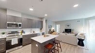 This well-appointed single-floor residence offers a thoughtfully designed open-concept layout that seamlessly connects the kitchen, dining, and living areas. The kitchen is a standout feature, showcasing dark taupe flat-front cabinetry extending to the ceiling, white quartz countertops, a classic subway tile backsplash, and a full suite of stainless steel appliances including a refrigerator, range, dishwasher, and built-in microwave. A central kitchen island with bar seating provides additional prep space and casual dining. Light hardwood-style flooring flows throughout the main living areas, enhancing the bright, airy atmosphere created by recessed lighting and neutral wall tones. The living room offers generous space for relaxation, while the adjacent dining area benefits from a sliding glass door that opens onto a private balcony with outdoor seating. Both bedrooms are comfortably sized with large windows that invite natural light, and light hardwood-style flooring. The two bathrooms are finished with clean white subway tile surrounds, white quartz vanity tops, and dark wood cabinetry. One bathroom features a walk-in shower, while the other includes a full soaking tub and shower combination, providing versatility for residents.
