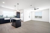 This well-appointed single-floor residence offers three bedrooms, two bathrooms, and a thoughtfully designed open-concept layout. The combined kitchen and living area serves as the heart of the home, featuring light hardwood-style flooring, bright white walls, and multiple windows that flood the space with natural light. A ceiling fan adds comfort to the living area, which flows seamlessly into the kitchen.

The kitchen is a standout, boasting a two-tone design with dark lower cabinets and white upper cabinets, a striking aqua glass tile backsplash, quartz countertops, stainless steel appliances, and a farmhouse-style sink positioned beneath a large window with outdoor views. A center island with pendant lighting provides additional prep and seating space.

The bedrooms feature plush carpeting, ceiling fans, and windows offering exterior views. The generously sized primary bedroom connects to a well-equipped bathroom with dark wood vanity, vessel sink, illuminated mirror, and matte black fixtures, alongside a separate walk-in shower and soaking tub clad in marble-style tile. A dedicated walk-in closet completes the primary suite. A second full bathroom mirrors the refined aesthetic. The hallway utility area includes an in-unit washer and dryer with additional shelving storage.