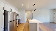 Located at 3200 Northwoods Rd in Saukville, WI, this thoughtfully designed one-bedroom, one-bathroom unit offers a clean, modern aesthetic throughout its efficiently organized single-floor layout. The open-concept kitchen and living area serves as the heart of the unit, featuring warm hardwood-style flooring, recessed lighting, and a contemporary pendant light fixture above the kitchen island. The kitchen is well-appointed with white shaker cabinetry, a full suite of stainless steel appliances including a refrigerator, microwave, and range, and a spacious island with a built-in sink and white countertops — ideal for both meal preparation and casual dining. The living area extends toward a sliding glass door that opens to a private balcony, allowing natural light to fill the space and offering pleasant outdoor views of the surrounding landscape. The bedroom is a comfortable, carpeted retreat with a dedicated window that brings in additional natural light. The bathroom features light wood-style flooring, a white vanity with a large mirror, chrome fixtures, and a glass-enclosed shower. A closet provides practical storage, completing this well-designed, move-in-ready unit.
