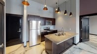 Located at 204 E Grand Ave in Eau Claire, Wisconsin, this single-floor space blends contemporary design with industrial character. Throughout the unit, polished marble-effect epoxy flooring creates a dramatic visual centerpiece, its sweeping grey and cream veining tying each room together cohesively.

The kitchen is a standout, featuring dark espresso cabinetry, stainless steel appliances, and a granite-topped island with an undermount sink. Pendant lights with warm copper interiors hang above, complementing the industrial aesthetic carried through exposed galvanized ductwork along the ceilings.

Multiple rooms offer versatile open layouts, bathed in natural light through large black-framed windows that provide views of the surrounding Eau Claire cityscape. Walls are finished in cool grey and muted lavender tones, lending a modern, calming atmosphere throughout.

The bathrooms are elegantly appointed with dark vanity cabinetry, granite countertops, round mirrors, and the same stunning marble-effect flooring. Dark-stained Craftsman-style interior doors with modern hardware provide a refined contrast to the lighter walls and floors.

Exposed brick accenting in the living/dining area adds warmth and a nod to the building's historic character, rounding out a space that masterfully balances industrial and contemporary design elements.