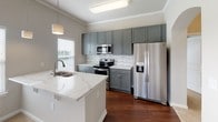This thoughtfully designed single-floor home offers a seamless blend of comfort and functionality throughout its well-proportioned layout. The open-concept living and dining area is bright and airy, filled with natural light streaming through multiple windows with classic blinds, and is finished with plush neutral carpeting and crown molding that adds a refined architectural touch. A ceiling fan overhead enhances the room's comfort and airflow.

The kitchen is a standout feature, showcasing slate-gray shaker-style cabinetry, a striking marble-look quartz peninsula with an undermount sink, and a coordinating tile backsplash. Stainless steel appliances — including a refrigerator with ice dispenser, range, microwave, and dishwasher — complete the space, while pendant lighting and rich hardwood flooring add warmth and style.

The bedrooms are generously sized, each with plush carpeting, ceiling fans, and ample natural light. One bedroom features a tray ceiling and curved walls, lending an elegant architectural detail. Walk-in closets with wire shelving provide practical storage solutions.

The bathrooms include a full bath with a soaking tub and shower combo, and a primary bath featuring a glass-enclosed walk-in shower with built-in shelving and brushed nickel fixtures. A dedicated laundry room with side-by-side washer and dryer and overhead wire shelving rounds out this well-equipped home.