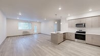 Located at 12608 E Nora Ave in Spokane Valley, WA, this modern 1-bedroom, 2-bathroom unit offers a thoughtfully designed open-concept floor plan with clean, contemporary finishes throughout. Light-toned luxury vinyl plank flooring extends across the main living areas, enhancing the bright and airy atmosphere created by recessed lighting and natural light from large windows.

The kitchen is a standout feature, showcasing an L-shaped layout with taupe wood-grain cabinetry reaching to the ceiling, white quartz countertops, a peninsula with an integrated sink, and a full suite of stainless steel appliances including a refrigerator, electric range, and over-the-range microwave. Stylish pendant lights hang above the peninsula, adding a modern touch. The kitchen flows seamlessly into the spacious living area, making the space well-suited for everyday living and entertaining.

The bedroom is carpeted for comfort and offers a generous walk-in closet equipped with wire shelving and hanging rods for ample storage. Both bathrooms reflect the same contemporary aesthetic, featuring wood-grain vanities with white countertops and light plank flooring. The unit is rounded out by a dedicated wall-mounted HVAC unit in the living area, providing year-round climate control.