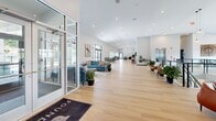 Located at 7207 McKnight Rd in Pittsburgh, PA, this expansive single-floor amenity space offers nearly 4,800 square feet of thoughtfully designed, multi-functional areas suited for socializing, working, and recreation. The grand entrance opens into a bright, open corridor with light hardwood flooring, soaring ceilings, and recessed lighting that runs the length of the space. A welcoming lounge area features plush seating, curated artwork, and lush indoor greenery, anchored by a striking double-sided brick fireplace with a mounted flat-screen display. Large floor-to-ceiling windows flood the interior with natural light while framing scenic views of the surrounding wooded landscape. The game and entertainment room includes a pool table, wall-mounted TV, pendant lighting, and casual seating arrangements for gatherings. A fully equipped kitchen showcases a bold blue island with quartz countertops, stainless steel appliances, warm wood cabinetry, and cascading hanging plants that add a vibrant, organic touch. A dedicated conference room with patterned carpet, a round table, and an industrial-style chandelier provides a professional setting for meetings. An elevator and well-appointed corridors round out this polished, modern community space.