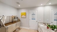 Located at 3131 Mountain Creek Rd in Chattanooga, TN, this compact yet highly functional pet grooming suite is designed with both efficiency and aesthetic appeal in mind. The space is organized across two connected rooms, each serving a distinct purpose within the grooming workflow.

The primary grooming area houses a professional-grade stainless steel pet bathing tub, complete with adjustable restraint arms and a built-in ramp for easy pet access. Light hardwood flooring and soft gray walls create a clean, calming environment, while recessed ceiling lighting ensures bright, even illumination throughout.

Adjacent to the grooming tub area is a well-finished vanity room featuring white cabinetry topped with speckled granite countertops, an undermount sink with a brushed nickel faucet, and a large wall mirror. Paper towel dispensers are conveniently mounted near the sink, underscoring the space's practical, professional design.

Decorative artwork adorns the walls in both rooms, adding warmth and a refined touch to what is otherwise a utilitarian space. A paneled white door with posted Arcadia guidelines connects the two areas and opens to the adjoining room. The overall design balances functionality with a polished, upscale finish, making this grooming suite a standout amenity within the Arcadia community.