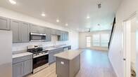 Located at 130 N Cedar St in Centerton, Arkansas, this two-story, 2-bedroom, 2-bathroom home is thoughtfully designed with modern finishes throughout. The main floor features an open-concept kitchen and living area with light hardwood-style flooring, recessed lighting, and a ceiling fan. The kitchen is a standout, boasting gray shaker-style cabinetry, granite countertops, stainless steel appliances including a range, microwave, dishwasher, and refrigerator, plus a central island for added prep and seating space. The adjacent living area is bright and airy, with a ceiling fan and a glass door leading to a private balcony. A staircase with decorative metal balusters connects the two equally sized floors. The upper level houses both bedrooms, each with ceiling fans, closets, and windows providing natural light and neighborhood views. The bathrooms are finished with gray vanities, granite countertops, and brushed nickel fixtures, with one featuring a full soaking tub. Additional conveniences include a dedicated laundry area, multiple closets for ample storage, and a hallway connecting the upper-level rooms. The home presents a clean, contemporary aesthetic throughout.