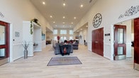 Located at 801 Olympic Square in Aberdeen, Maryland, this single-story community clubhouse for the Residences of Summerlin offers a well-appointed, open-concept layout designed to serve residents across a variety of social and functional needs. The grand entrance foyer sets an impressive tone with soaring ceilings, recessed lighting, and light wood-style flooring that flows seamlessly throughout the main gathering areas. The expansive main lounge features multiple seating arrangements, including plush sofas and accent chairs, centered around a wall-mounted television and complemented by decorative built-in shelving. A large decorative clock anchors the entryway, adding a striking architectural detail. Adjacent to the main lounge, a bright dining area accommodates multiple table settings and benefits from abundant natural light streaming through oversized windows with vertical blinds. A secondary lounge provides a more intimate seating area with leather sofas and distinctive wall art. The facility also includes a dedicated conference room furnished with a large oval table and ergonomic seating, ideal for meetings or private gatherings. A full kitchen outfitted with rich cherry cabinetry, granite countertops, and stainless steel appliances rounds out the amenities, supporting catering and community events with ease.