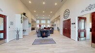 Located at 801 Olympic Square in Aberdeen, Maryland, this single-story community clubhouse for the Residences of Summerlin offers a well-appointed, open-concept layout designed to serve residents across a variety of social and functional needs. The grand entrance foyer sets an impressive tone with soaring ceilings, recessed lighting, and light wood-style flooring that flows seamlessly throughout the main gathering areas. The expansive main lounge features multiple seating arrangements, including plush sofas and accent chairs, centered around a wall-mounted television and complemented by decorative built-in shelving. A large decorative clock anchors the entryway, adding a striking architectural detail. Adjacent to the main lounge, a bright dining area accommodates multiple table settings and benefits from abundant natural light streaming through oversized windows with vertical blinds. A secondary lounge provides a more intimate seating area with leather sofas and distinctive wall art. The facility also includes a dedicated conference room furnished with a large oval table and ergonomic seating, ideal for meetings or private gatherings. A full kitchen outfitted with rich cherry cabinetry, granite countertops, and stainless steel appliances rounds out the amenities, supporting catering and community events with ease.