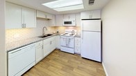 Located at 1600 S Valley View Blvd in Las Vegas, Nevada, this single-floor space offers a clean and functional layout designed for comfortable everyday living. The kitchen is a standout feature, showcasing white shaker-style cabinetry that extends to the ceiling, paired with granite countertops and a classic white subway tile backsplash that adds timeless character. A skylight panel in the ceiling floods the kitchen with bright, diffused light, creating an open and airy atmosphere. White appliances, including a refrigerator, electric range, built-in microwave, and dishwasher, are neatly integrated into the layout, providing a cohesive and practical cooking environment. The undermount sink is set beneath the countertop for a streamlined look, complemented by a modern arc faucet. Warm wood-look flooring runs throughout, adding a natural, inviting tone that contrasts beautifully with the crisp white cabinetry. The overall design reflects a bright, neutral aesthetic with thoughtful attention to detail, making the space feel both functional and welcoming.