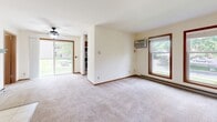 The Venice at 7705 Carrington Drive is a single-floor, 3-bedroom, 1-bathroom residence in Madison, Wisconsin, offering a practical and comfortable layout. The open living area features plush wall-to-wall carpeting, warm wood-trimmed windows that frame lush green outdoor views, a ceiling fan, and a sliding glass door that fills the space with natural light. A wall-mounted A/C unit and baseboard heating provide year-round climate comfort.

The generously sized primary bedroom is notably spacious and includes a large walk-in closet outfitted with built-in shelving and hanging rods, offering ample storage. The two additional bedrooms are well-proportioned, each featuring carpeted floors, wood-framed windows with outdoor views, and their own closets with hanging rods and shelving.

The bathroom is finished with tile flooring, a wood-cabinet vanity with a stone-look countertop, a large mirror, and a light fixture above. A dedicated laundry room includes a full-size washer and dryer alongside wire shelving for additional storage. Throughout the home, warm wood accents on doors and window trim, cream-toned walls, and consistent carpeting create a cohesive and inviting atmosphere.