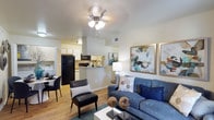 This 2-bedroom, 1-bathroom residence offers a well-designed single-floor layout that maximizes functionality and comfort. The open-concept living area serves as the heart of the home, featuring warm hardwood-style flooring, a ceiling fan with integrated lighting, and a neutral color palette that creates a bright and inviting atmosphere. A comfortable seating arrangement anchors the living space, complemented by tasteful wall art that adds a contemporary touch.

The kitchen connects seamlessly to the living area via a breakfast bar counter, providing both additional prep space and a casual dining option. Equipped with black appliances, including a full-sized refrigerator, microwave, and range, the kitchen also features white cabinetry that maximizes storage. A separate dining nook is situated adjacent to the kitchen, offering a dedicated space for meals.

The layout is thoughtfully designed to make efficient use of the available square footage, ensuring each area feels purposeful. Ample natural light flows throughout the space, enhancing the warm tones of the flooring and walls. The overall ambiance is modern yet cozy, making this a practical and welcoming home suitable for a variety of living arrangements.