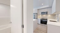 This thoughtfully designed 3-bedroom, 2-bathroom residence offers a modern aesthetic across a single floor, making efficient use of every square foot. The contemporary kitchen is a standout feature, showcasing flat-panel white cabinetry extending to the ceiling, a large waterfall-edge island with bright white quartz countertops, a stylish tile backsplash, and a full suite of stainless steel appliances including a French door refrigerator, electric range, built-in microwave, and dishwasher. Light wood-tone flooring flows seamlessly throughout the living areas and bedrooms, lending warmth to the crisp, white interior palette. The bedrooms are bright and clean-lined, with the primary bedroom offering a built-in closet with sliding doors and a generously sized window that invites natural light. The two bathrooms maintain the home's consistent modern design, each featuring a soaker tub and shower combination with a handheld fixture, white tile flooring, an integrated vanity with an undermount sink, and recessed lighting. The hallways connect each room with a clean, open flow. Overall, the space presents a fresh, minimalist character that is both functional and visually cohesive.